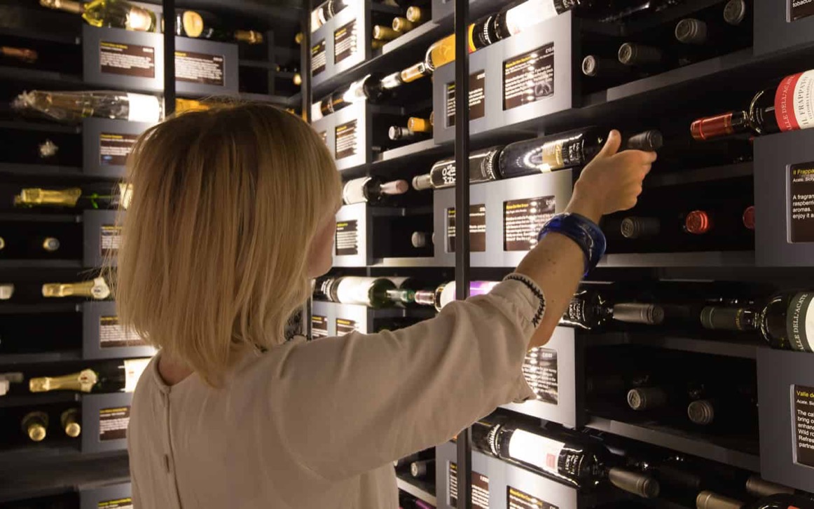 Oeno Wines customer browsing LED-lit modular racking with tasting notes against exposed stone wall